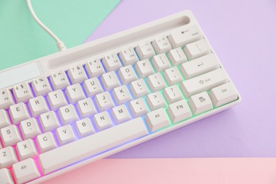Photo of Modern computer keyboard with RGB lighting on color background, above view