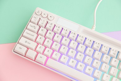Photo of Modern computer keyboard with RGB lighting on color background, above view