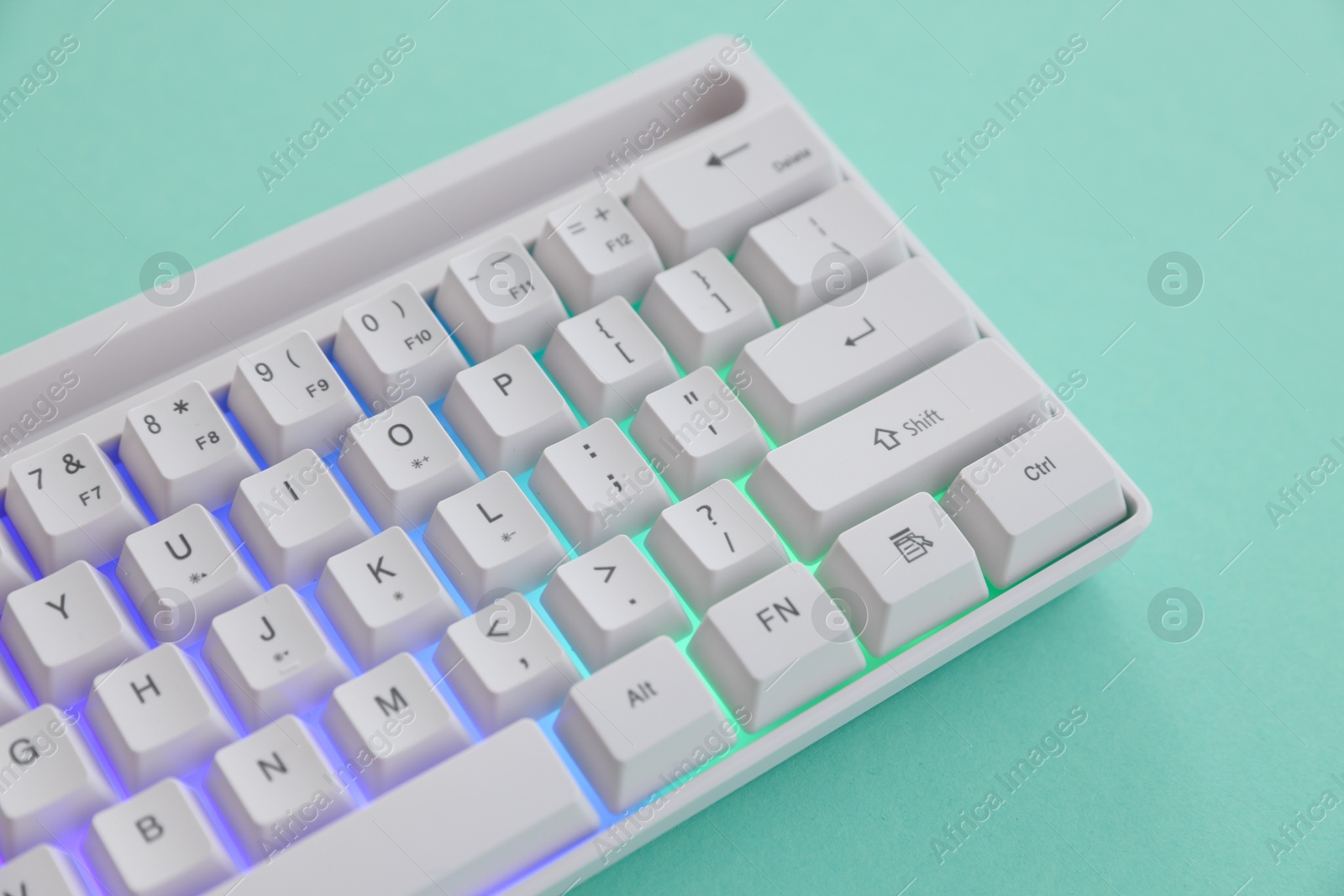 Photo of Modern computer keyboard with RGB lighting on turquoise background, above view