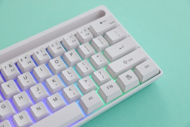 Photo of Modern computer keyboard with RGB lighting on turquoise background, above view