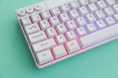 Photo of Modern computer keyboard with RGB lighting on turquoise background, above view