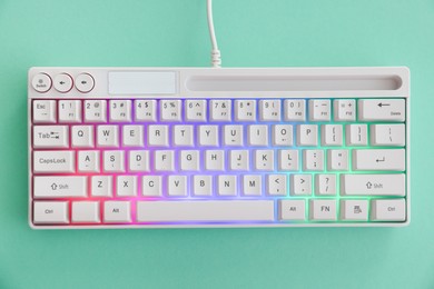 Photo of Modern computer keyboard with RGB lighting on turquoise background, top view