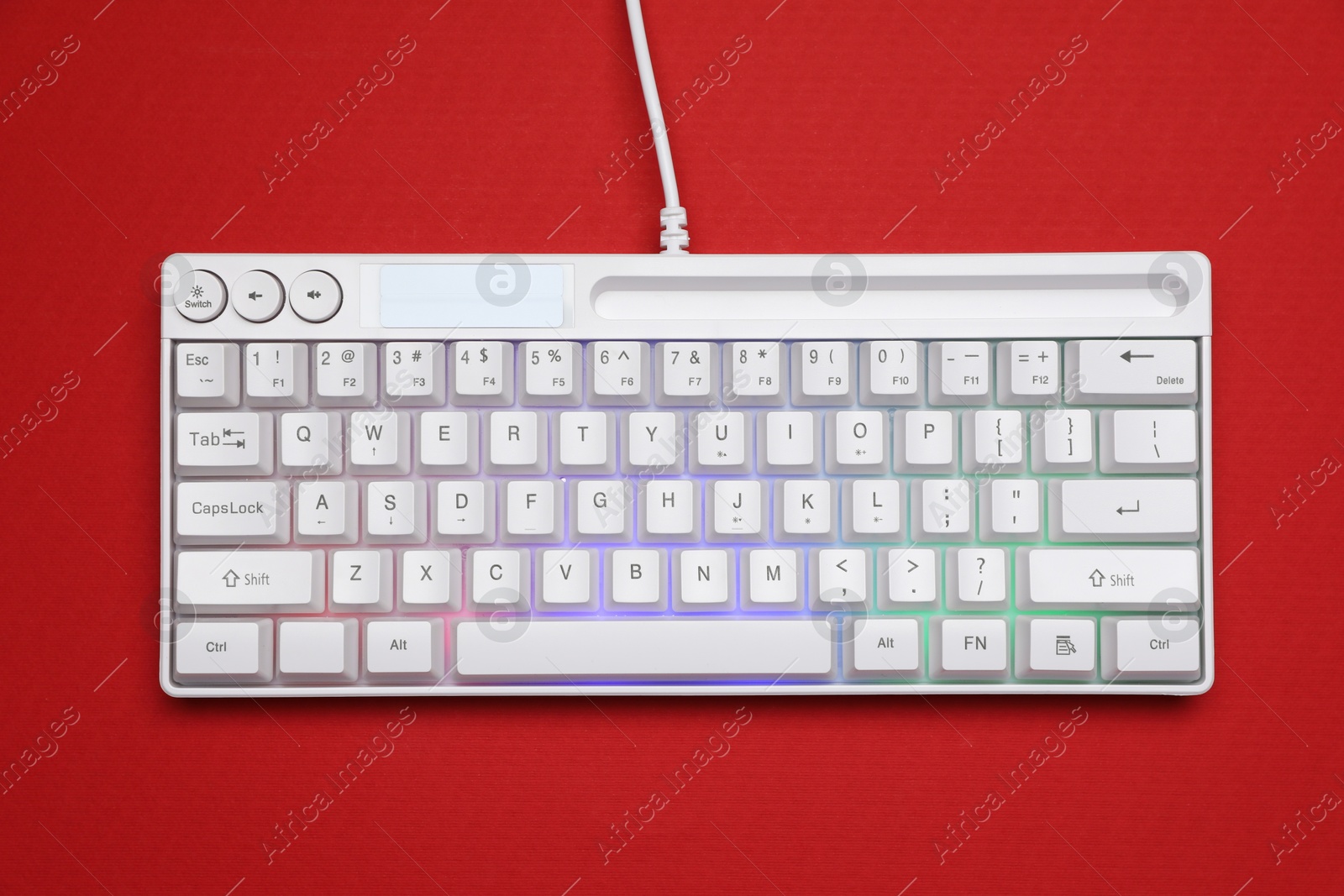 Photo of Modern white keyboard with RGB lighting on red background, top view