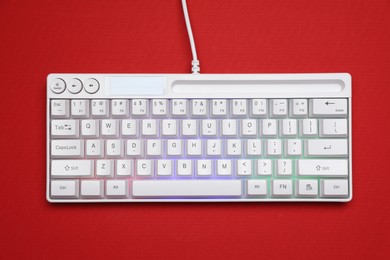 Photo of Modern white keyboard with RGB lighting on red background, top view