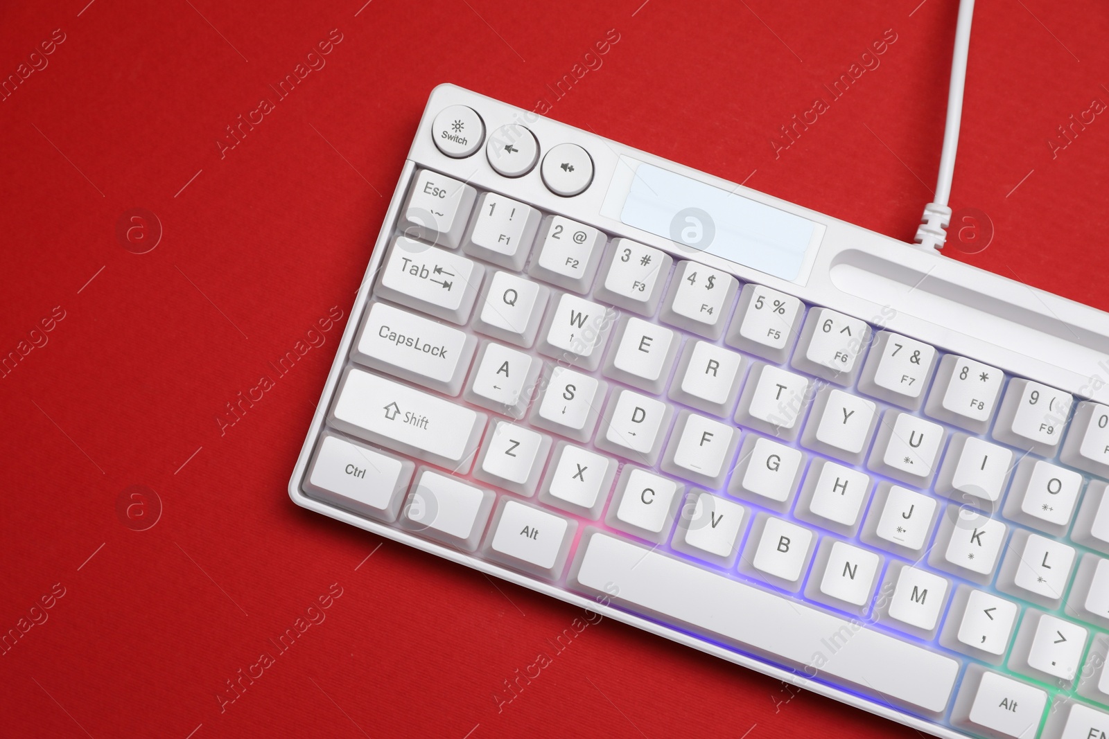 Photo of Modern white keyboard with RGB lighting on red background, top view