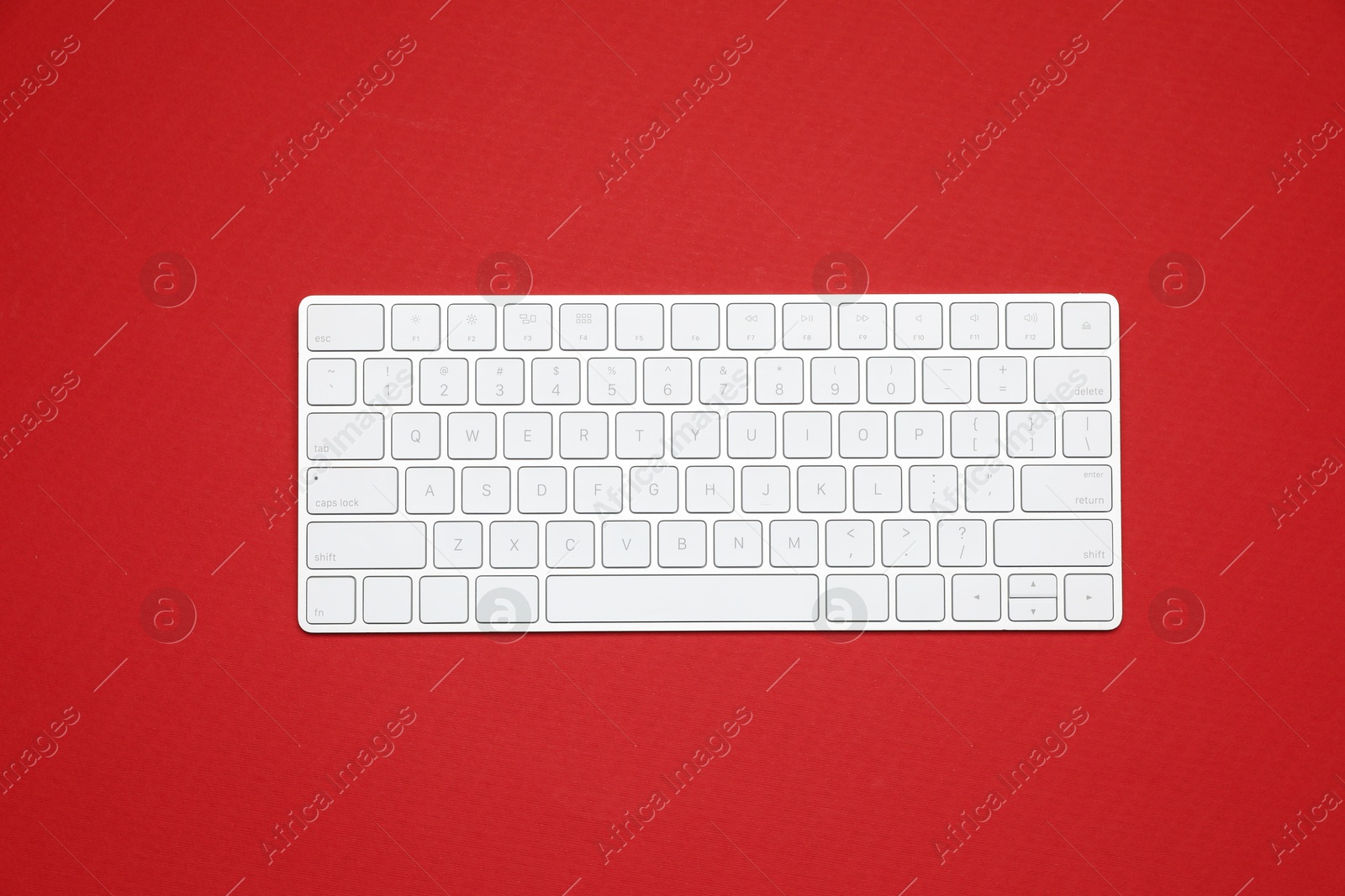 Photo of Modern white wireless keyboard on red background, top view