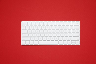 Photo of Modern white wireless keyboard on red background, top view
