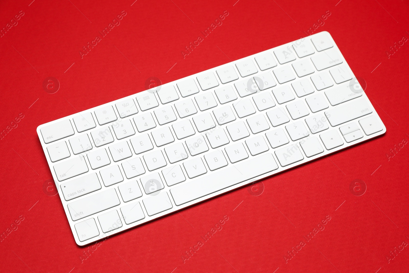Photo of Modern white wireless keyboard on red background