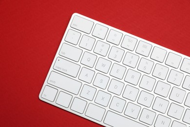 Photo of Modern white wireless keyboard on red background, top view