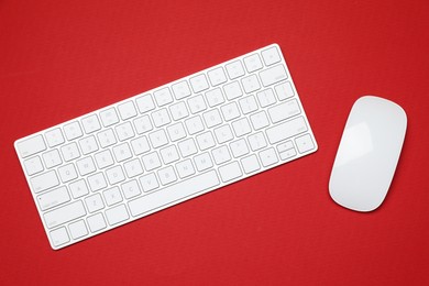 Photo of Modern white wireless keyboard and mouse on red background, top view
