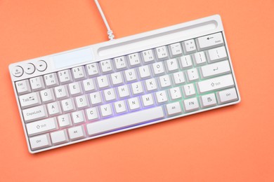 Photo of Modern white keyboard with RGB lighting on orange background, top view