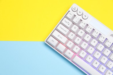Photo of Modern white keyboard with RGB lighting on color background, top view. Space for text