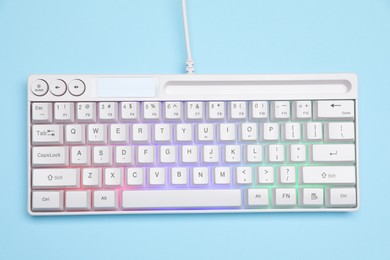 Photo of Modern white keyboard with RGB lighting on light blue background