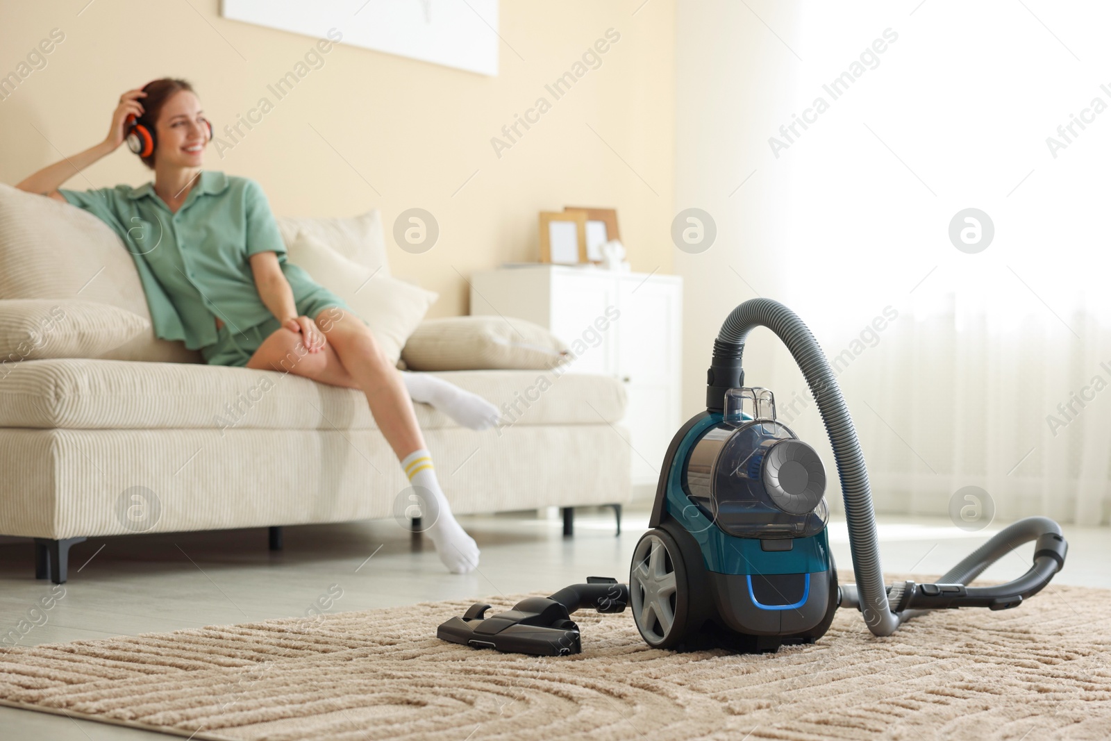 Woman in headphones resting on sofa at home, focus on vacuum cleaner Photo of Woman in headphones resting on sofa at home, focus on vacuum cleaner