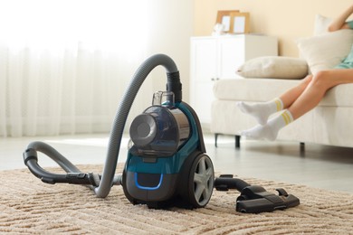 Photo of Woman resting on sofa at home, focus on vacuum cleaner