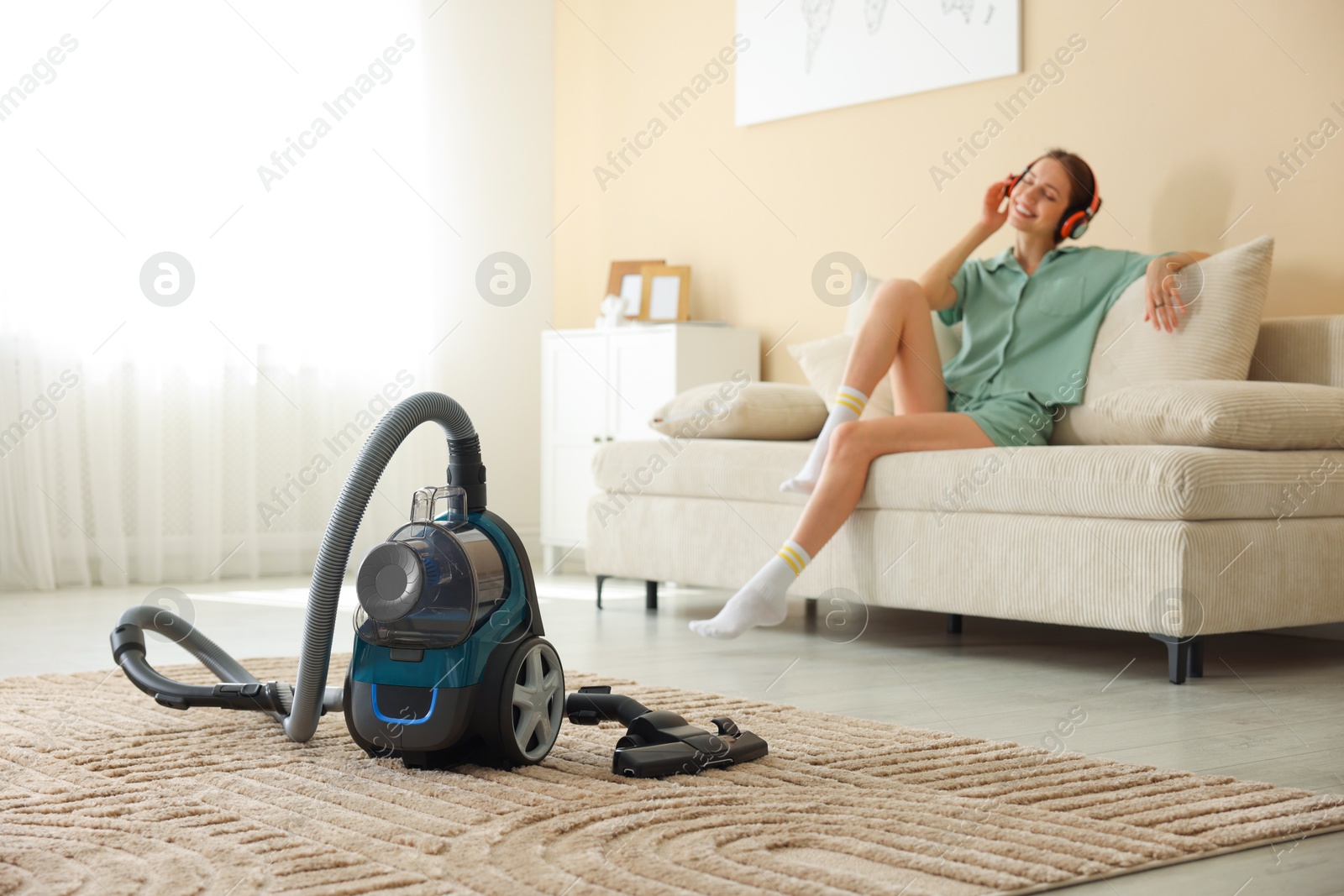 Woman in headphones resting on sofa at home, focus on vacuum cleaner Photo of Woman in headphones resting on sofa at home, focus on vacuum cleaner