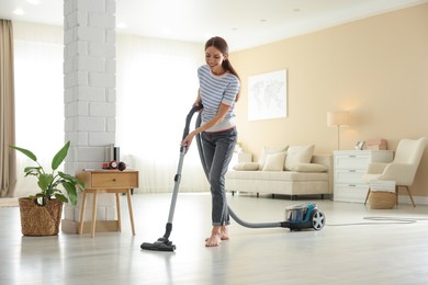 Photo of Woman cleaning floor with vacuum cleaner at home