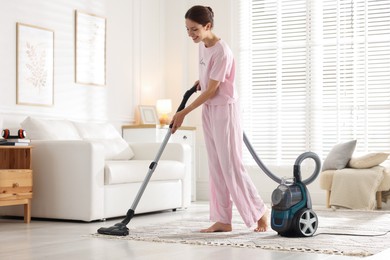 Photo of Woman cleaning carpet with vacuum cleaner at home