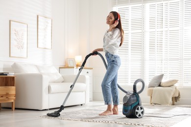 Photo of Woman in headphones cleaning carpet with vacuum cleaner at home