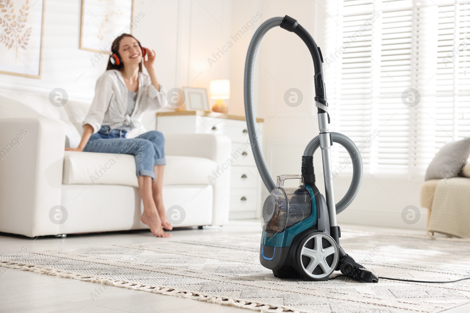 Woman in headphones resting on sofa at home, focus on vacuum cleaner Photo of Woman in headphones resting on sofa at home, focus on vacuum cleaner
