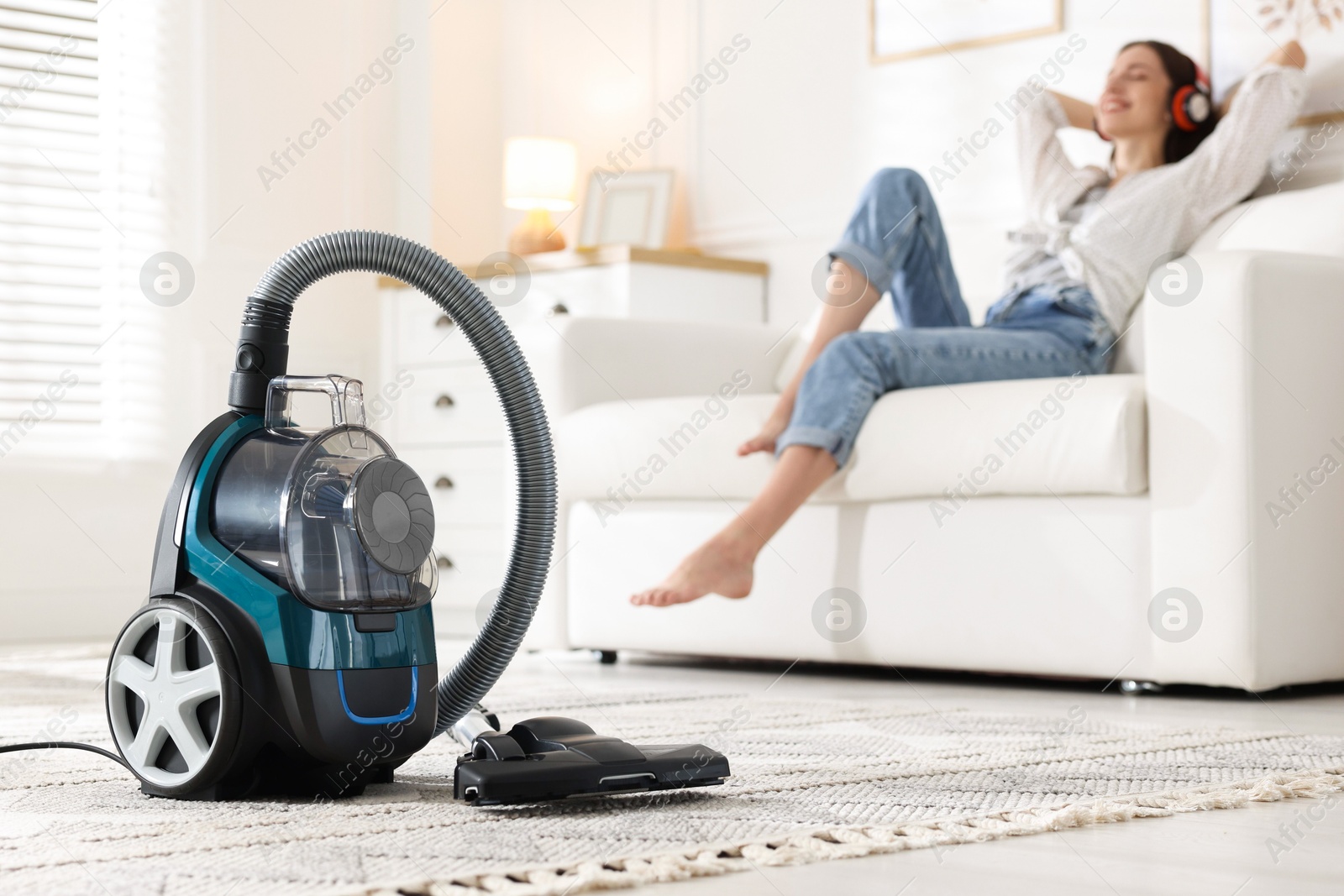 Woman in headphones resting on sofa at home, focus on vacuum cleaner Photo of Woman in headphones resting on sofa at home, focus on vacuum cleaner