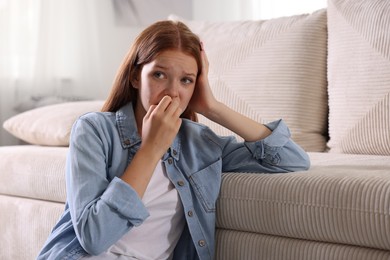 Photo of Teenage girl suffering from panic attack leaning on sofa at home
