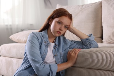 Photo of Teenage girl suffering from panic attack leaning on sofa at home