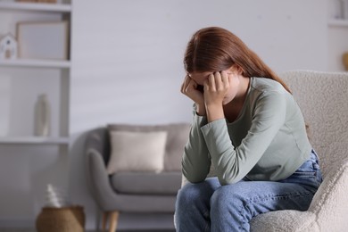 Photo of Teenage girl suffering from panic attack on armchair at home. Space for text