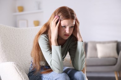 Photo of Teenage girl suffering from panic attack on armchair at home