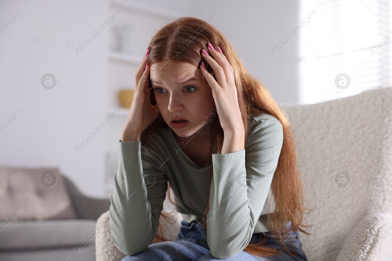 Teenage girl suffering from panic attack on armchair at home Photo of Teenage girl suffering from panic attack on armchair at home