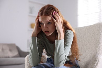 Photo of Teenage girl suffering from panic attack on armchair at home