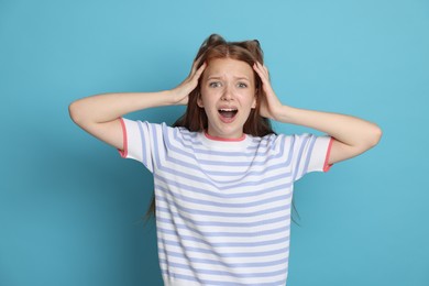 Photo of Teenage girl suffering from panic attack on light blue background