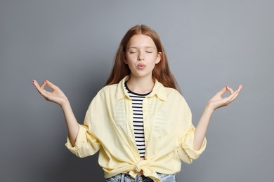 Photo of Teenage girl meditating on grey background. Way to stop panic attack