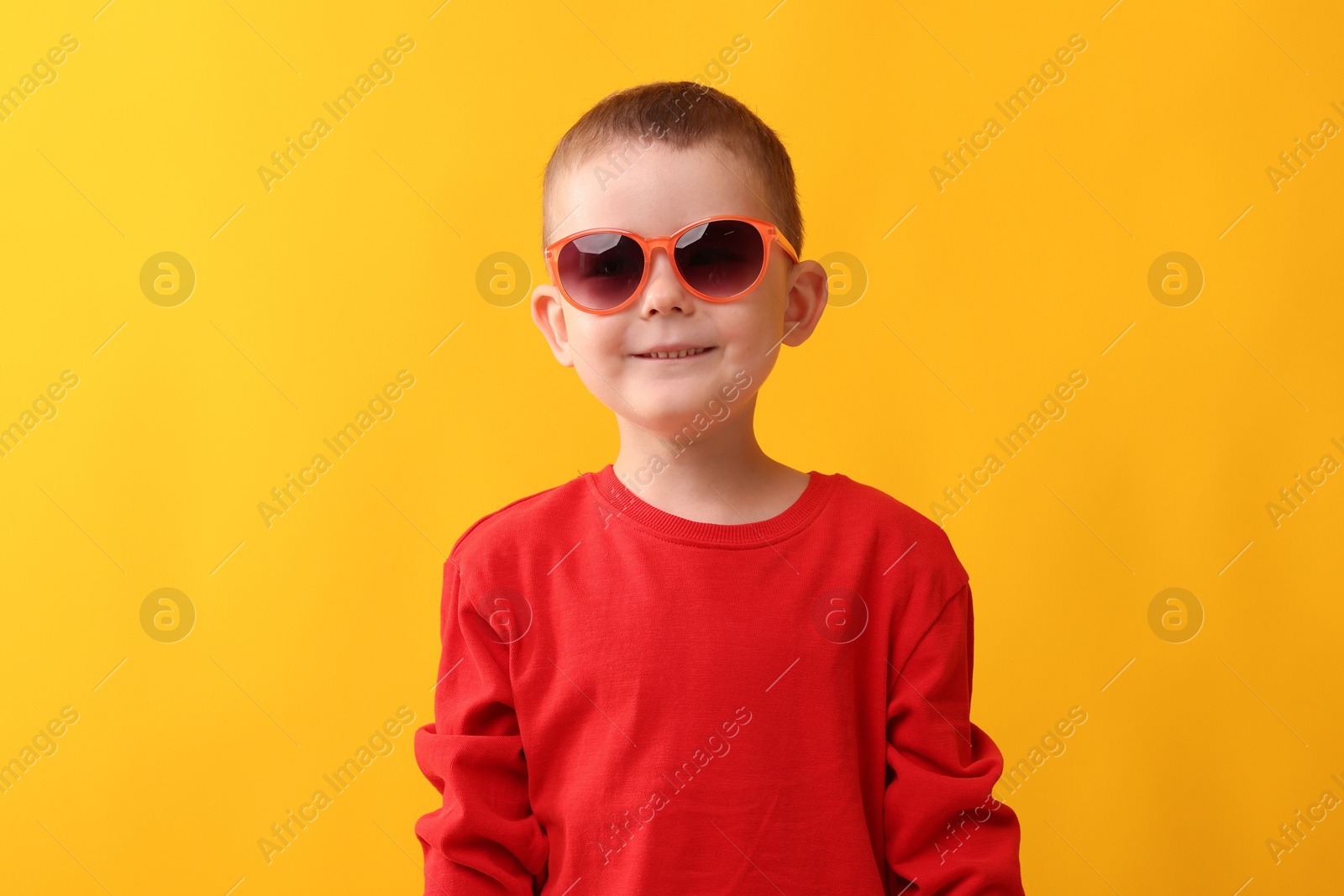 Cute little boy in sunglasses laughing on yellow background Photo of Cute little boy in sunglasses laughing on yellow background
