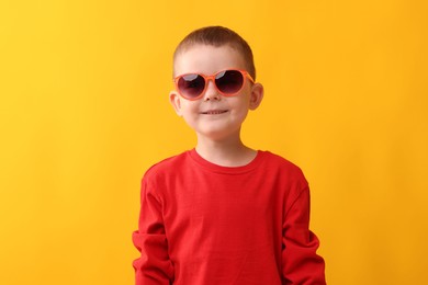 Photo of Cute little boy in sunglasses laughing on yellow background