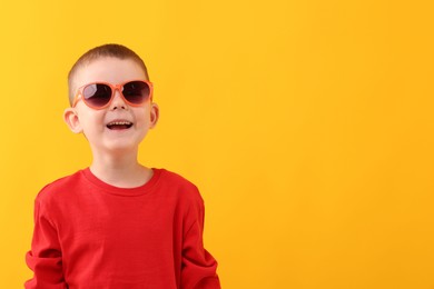 Photo of Cute little boy in sunglasses laughing on yellow background. Space for text
