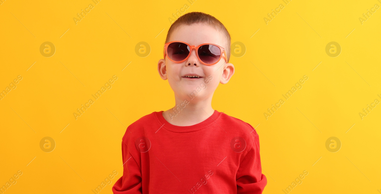Cute little boy in sunglasses laughing on yellow background Photo of Cute little boy in sunglasses laughing on yellow background