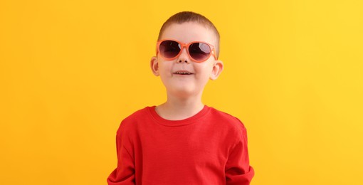 Photo of Cute little boy in sunglasses laughing on yellow background
