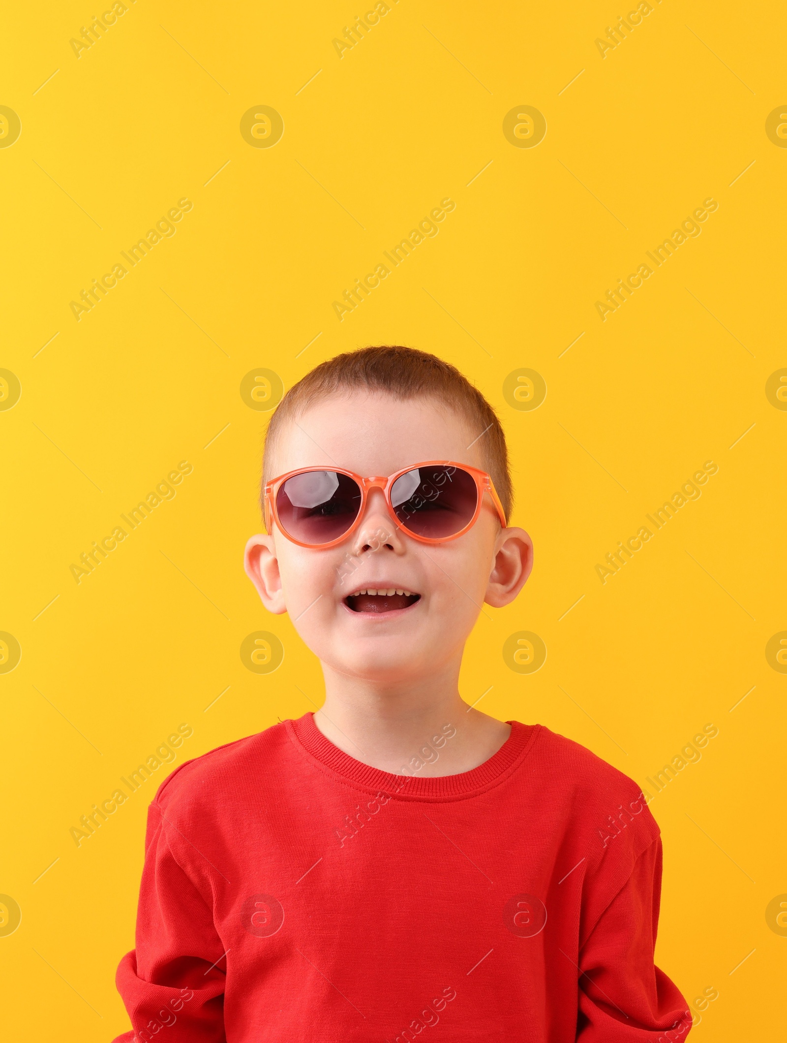 Photo of Cute little boy in sunglasses laughing on yellow background