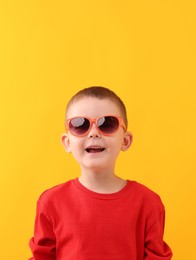Photo of Cute little boy in sunglasses laughing on yellow background