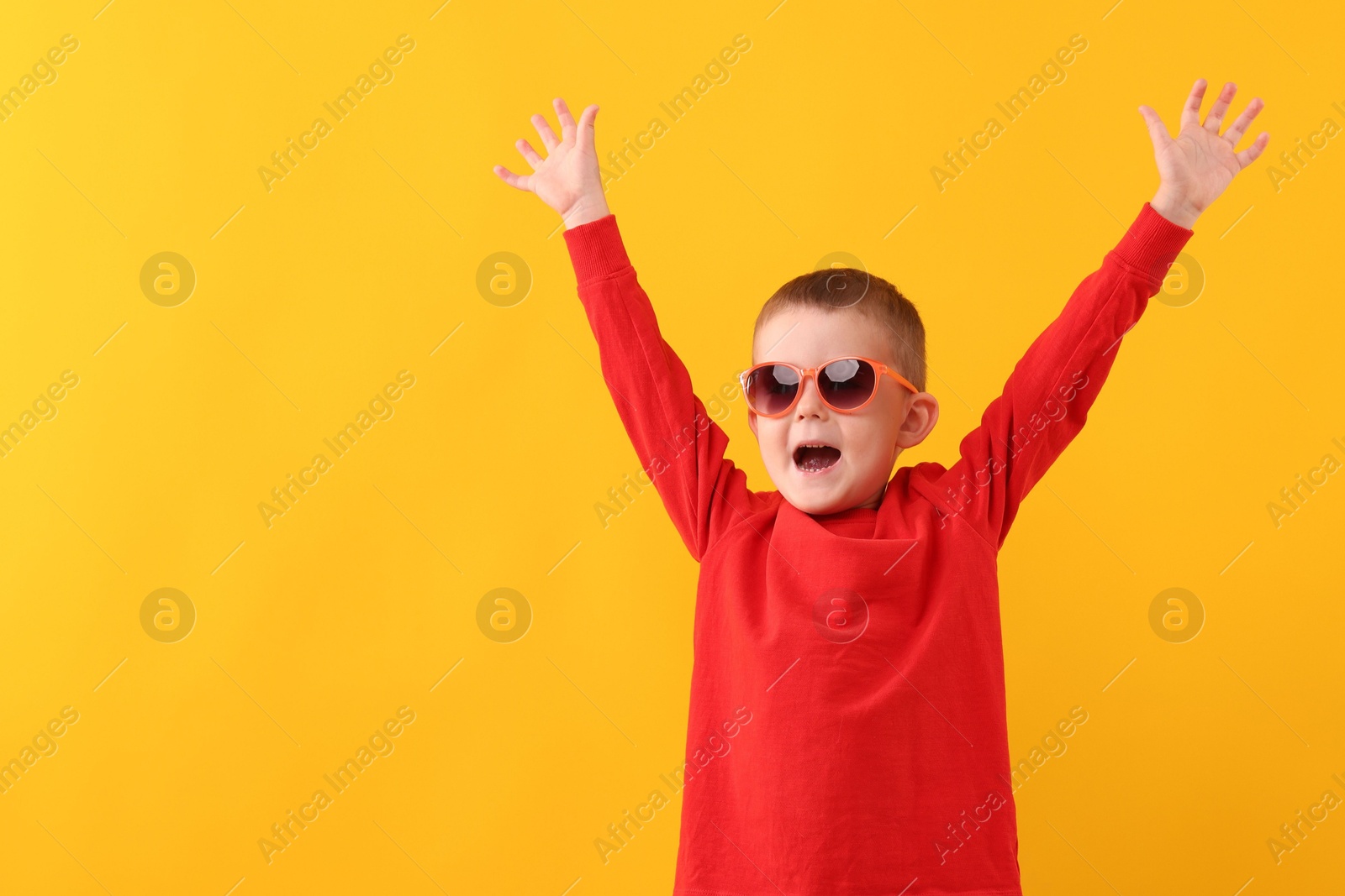 Cute little boy in sunglasses laughing on yellow background Photo of Cute little boy in sunglasses laughing on yellow background