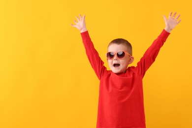 Photo of Cute little boy in sunglasses laughing on yellow background