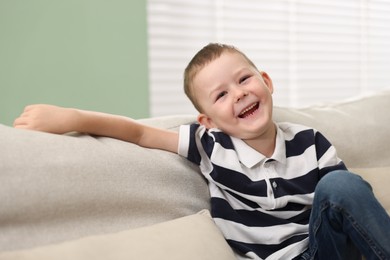 Photo of Cute little boy laughing on sofa at home