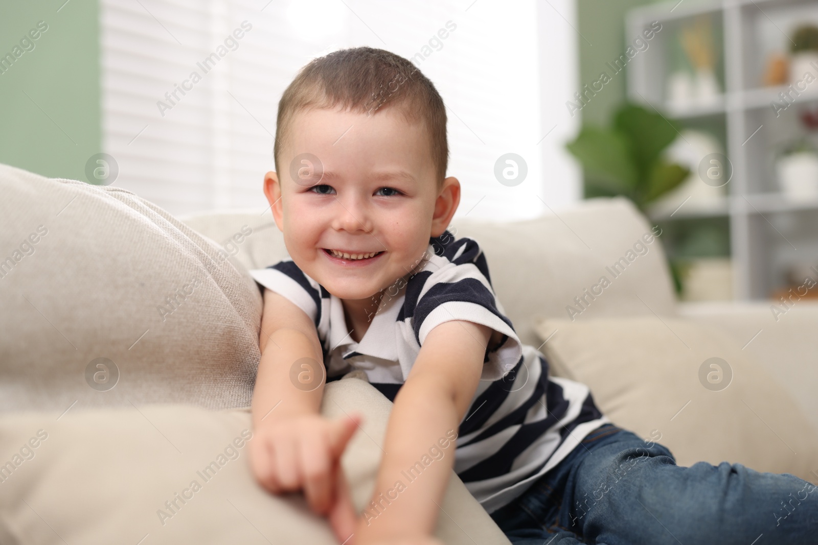 Cute little boy pointing and laughing at something on sofa indoors Photo of Cute little boy pointing and laughing at something on sofa indoors