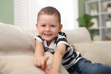 Photo of Cute little boy pointing and laughing at something on sofa indoors