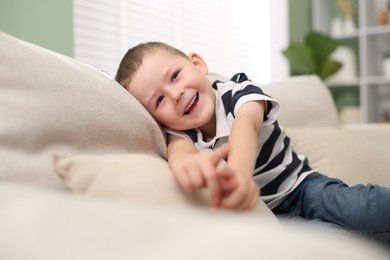 Photo of Cute little boy pointing and laughing at something on sofa indoors