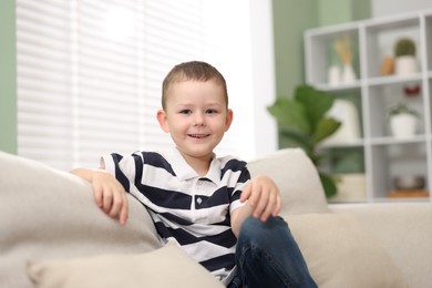 Photo of Cute little boy laughing on sofa at home