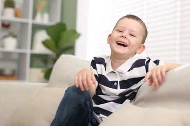 Photo of Cute little boy laughing on sofa at home. Space for text