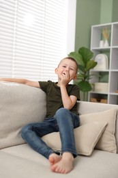 Photo of Cute little boy laughing on sofa at home