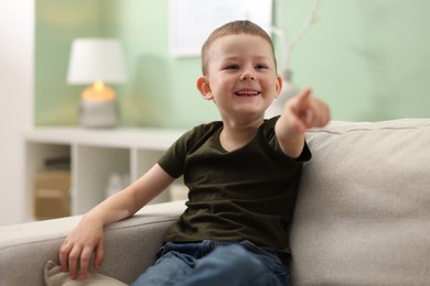 Photo of Cute little boy pointing and laughing at something on sofa indoors